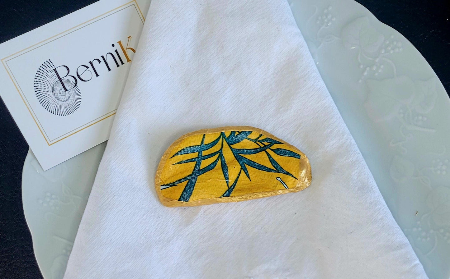 Apportez une touche de nature et d'élégance à vos repas avec ce porte couteau en coquille d'huître recyclée, orné de feuilles de bambou vertes sur fond moutarde.