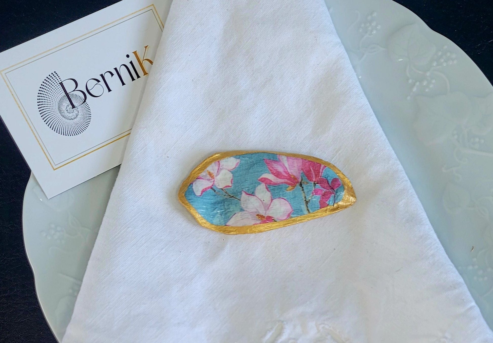 Apportez une touche printanière à votre table avec ce porte couteau magnolia, ornée de fleurs délicates et fond bleu tendre, en coquille recyclée avec finition dorée.