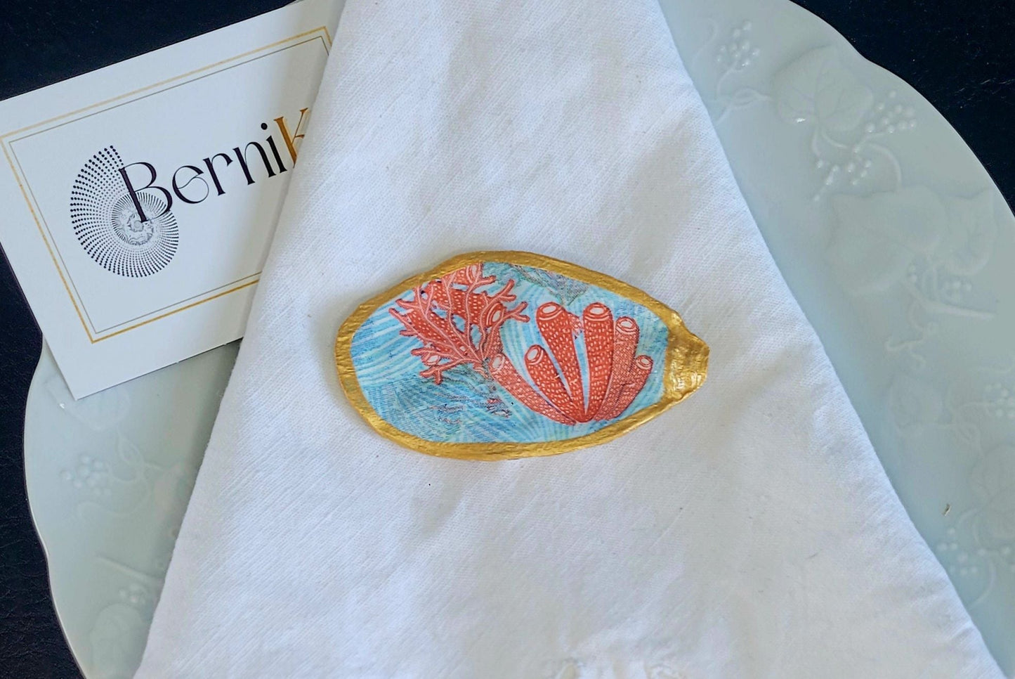 Apportez une touche sous-marine à votre table avec ce porte couteau aux coraux orangés et eaux bleues, en coquille recyclée et finition dorée peinte à la main.