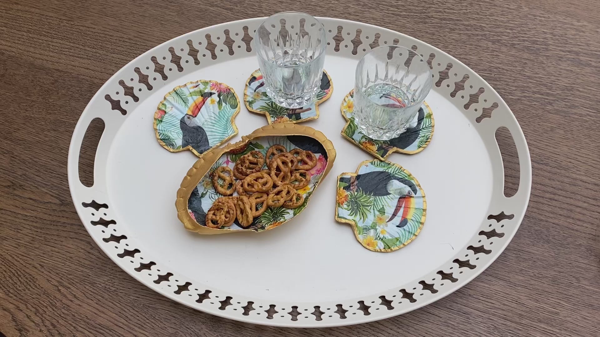 Des sous-verres uniques en coquilles Saint-Jacques, décorés à la main avec un liseré doré et un motif toucan vibrant, apportant une touche tropicale et élégante à votre table.