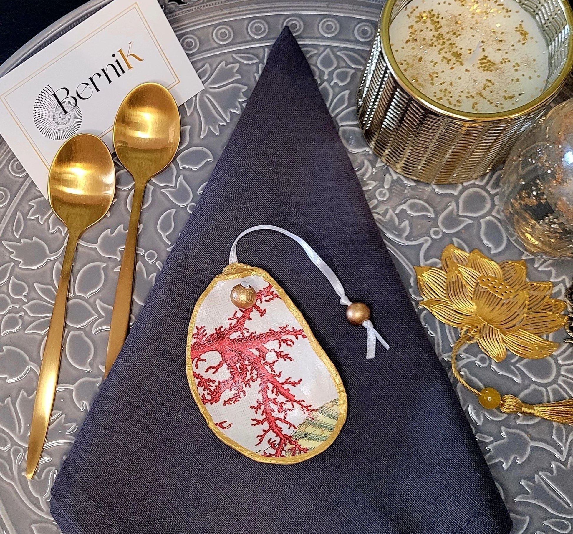 Décoration de table sophistiquée : coquilles d’huître avec motifs corail rouge et rubans élégants, charme naturel garanti.