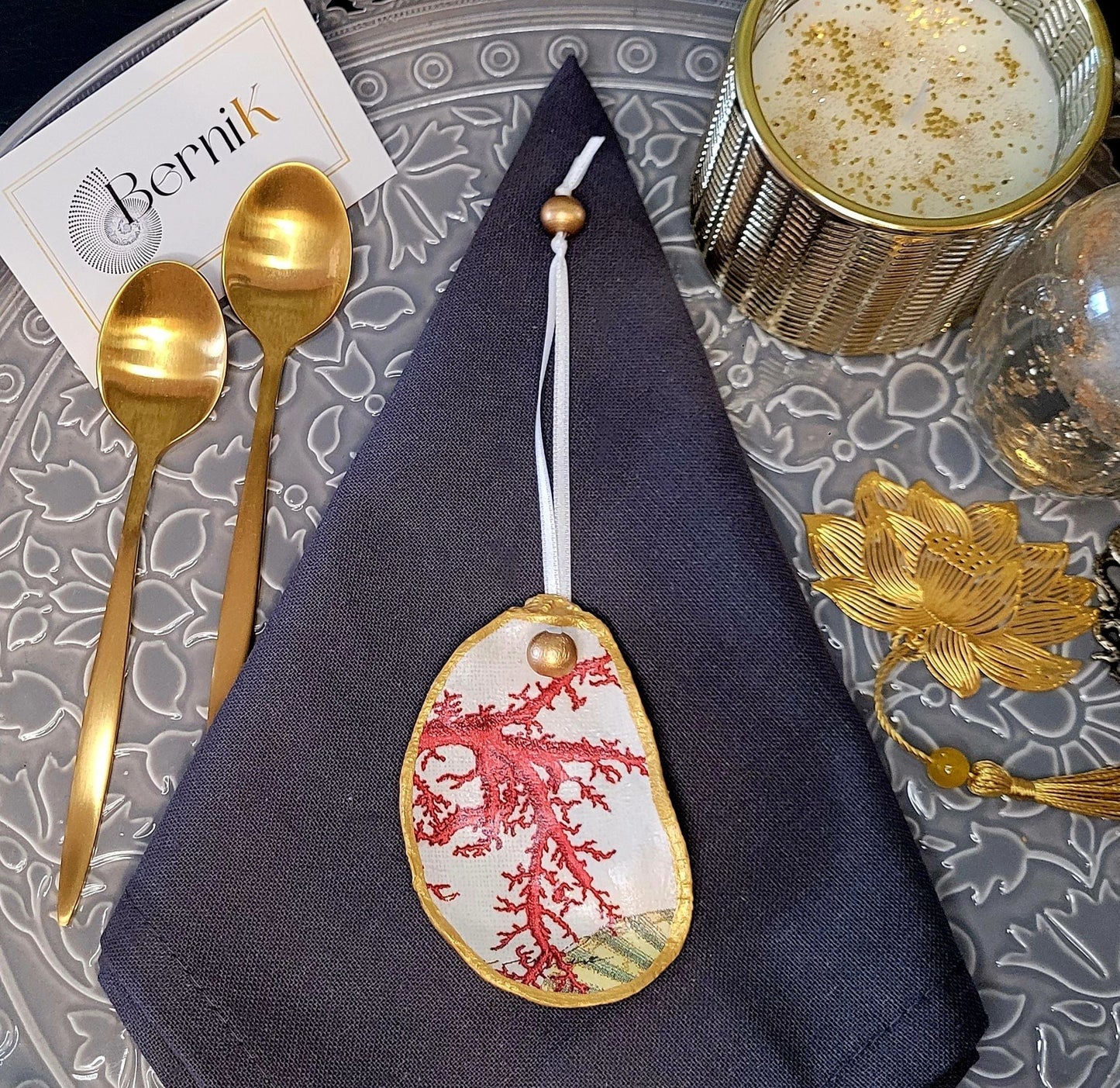 Accessoires de table artisanaux : coquilles d’huître décorées de motifs corail rouge et perles dorées en bois naturel.